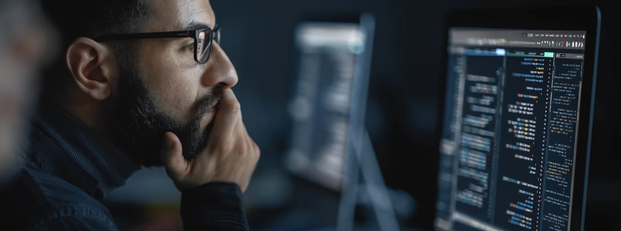 Man focused on computer screens displaying code, symbolizing programming or software development.