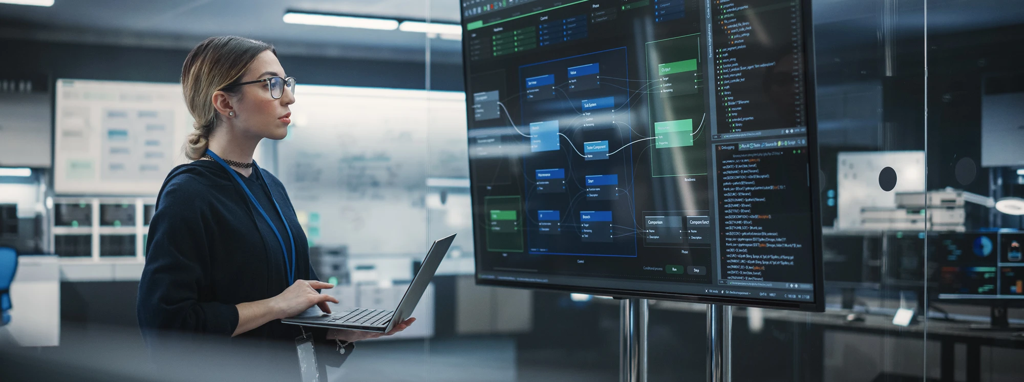 Tech professional analyzing software on a large screen with a laptop in a modern office.