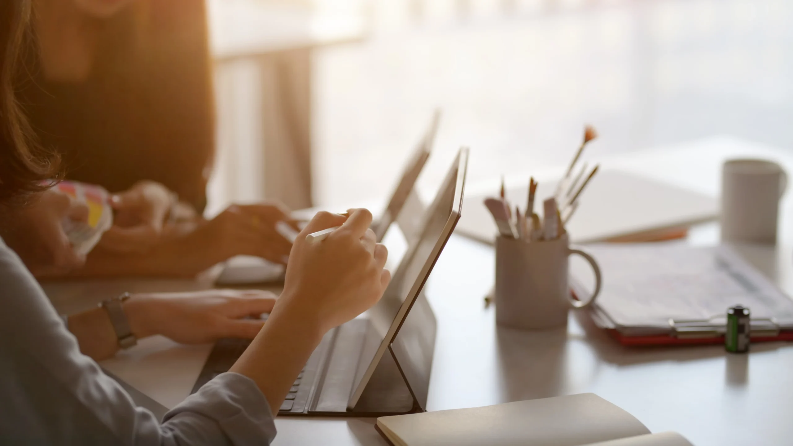 People collaborating on tablets in a bright office, surrounded by stationery and notebooks.