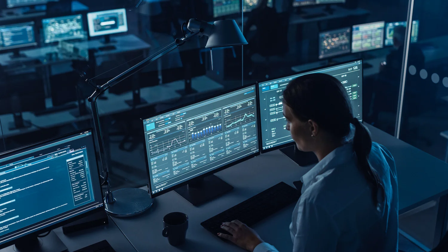 Person analyzing data on multiple computer screens in a dimly lit operations center.