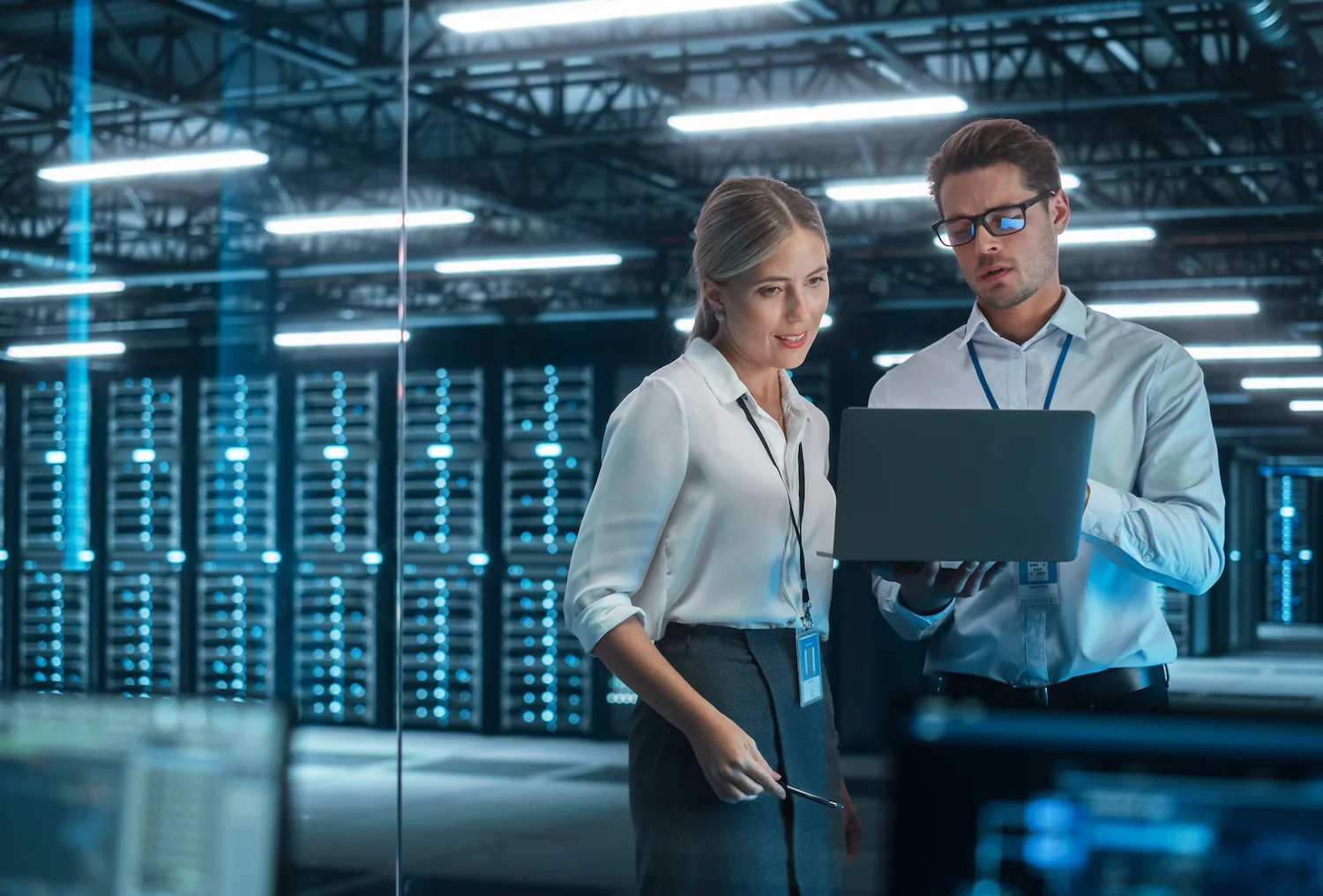 Two professionals analyzing data on a laptop in a modern server room.