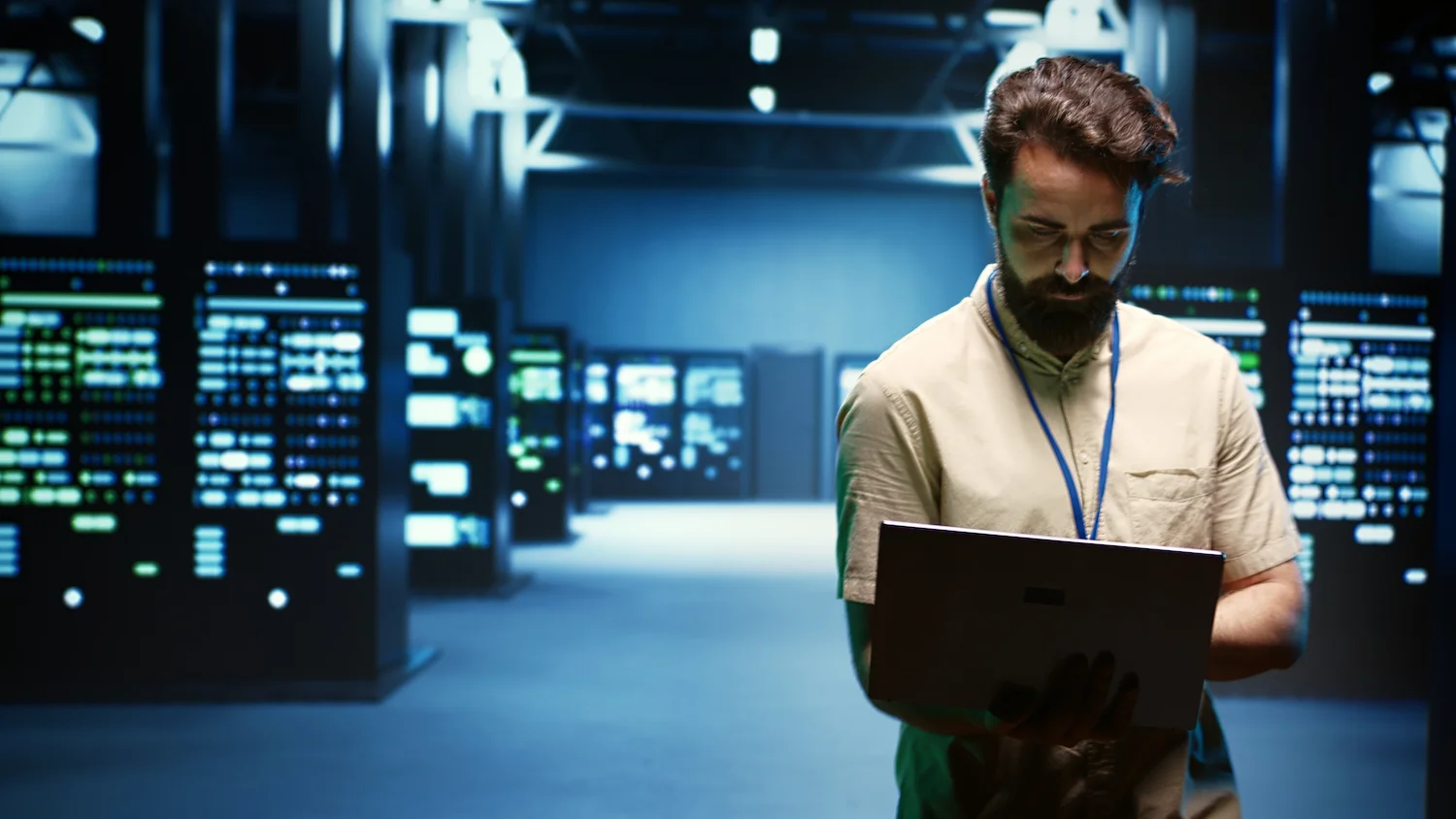 Technician with laptop in a data center surrounded by illuminated server racks.