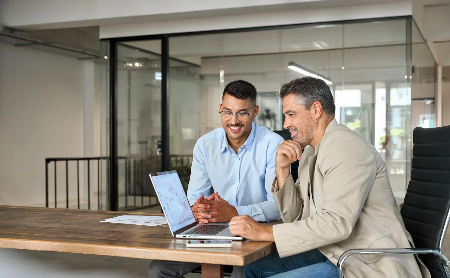 Two business professionals discussing data on a laptop in a modern office setting.