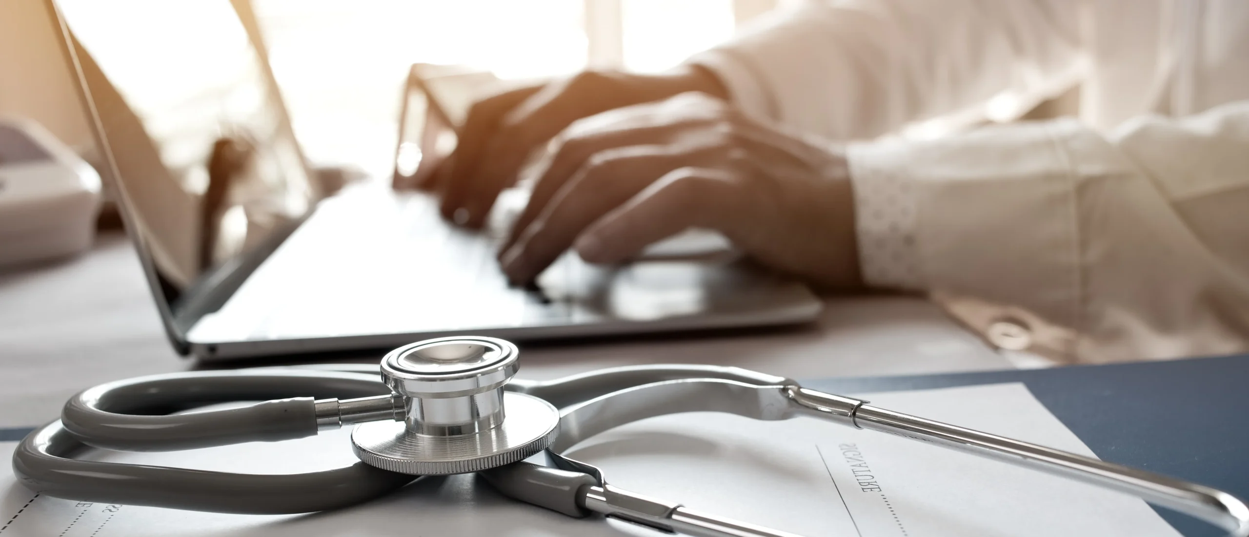 Doctor typing on laptop with stethoscope on desk, symbolizing healthcare and digital technology integration.